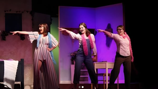 Drei Schülerinnen der Morro Bay High School tanzen auf der Bühne vor einem violetten Hintergrund.