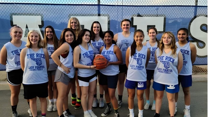 Eine Gruppe junger Basketballspielerinnen der Morro Bay High School steht zusammen auf einem Außenspielplatz mit Stadtblick.