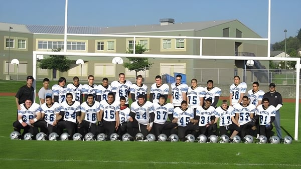 Eine Gruppe Schüler in Fussballuniformen posiert auf dem Sportfeld vor dem Schulgebäude der Moscrop School.
