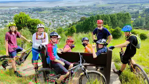 Eine Gruppe von Schülerinnen und Schülern der Motueka High School in bunter Fahrradausrüstung posiert auf einem Bergweg mit Blick auf die Stadt im Hintergrund.
