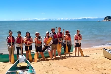 Eine Gruppe Schülerinnen und Schüler der Motueka High School steht am Strand mit einer felsigen Insel im Hintergrund.