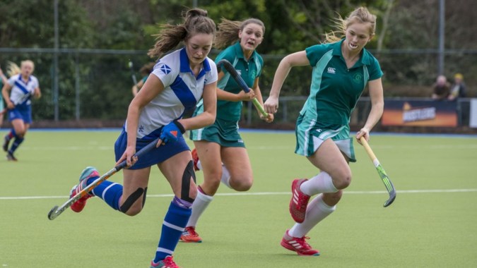 Eine Gruppe von Schülerinnen der Mount Anville Secondary School spielt Feldhockey auf einem Kunstrasenplatz.