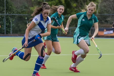 Schülerinnen der Mount Anville Secondary School spielen ein Hockeyspiel auf einem Sportplatz mit Zaun.