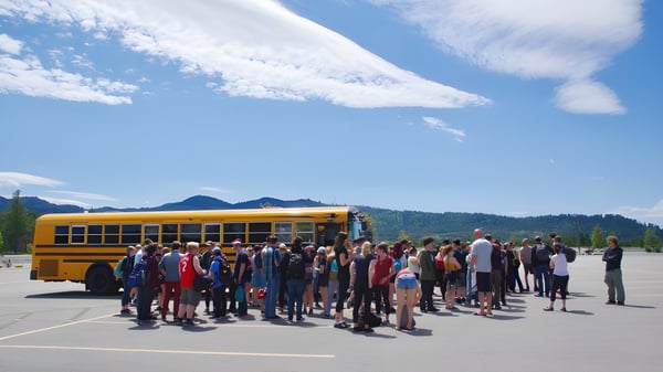Schüler der Mount Baker Secondary School stehen vor einem gelben Schulbus mit Bergen und blauem Himmel im Hintergrund.