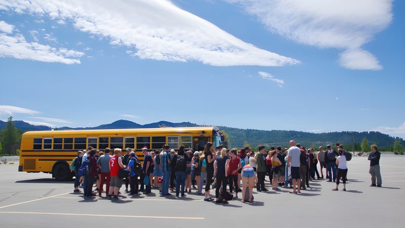 Schüler der Mount Baker Secondary School stehen vor einem gelben Schulbus mit Bergen und blauem Himmel im Hintergrund.