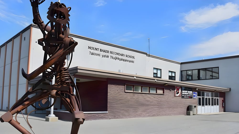 Eine große Metallskulptur einer skelettartigen Figur steht vor dem modernen Gebäude der Mount Baker Secondary School.