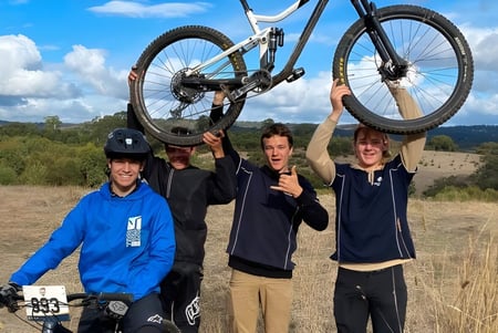 Schüler der Mount Barker High School halten ein Mountainbike auf einer hügeligen Wiese mit bewölktem Himmel.
