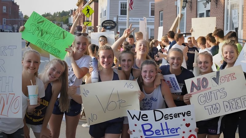 Schülerinnen und Schüler der Mount Blue High School versammeln sich auf einer Straße und halten Schilder mit politischen Botschaften.