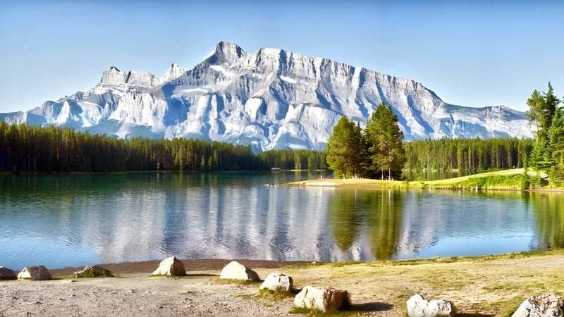 Ein ruhiger Bergsee mit schneebedeckten Gipfeln und bewaldetem Ufer nahe der Mount Boucherie Secondary School.