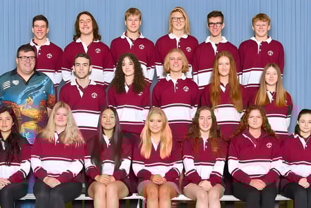 Eine Gruppe Schülerinnen und Schüler der Mount Compass Area School posiert in passenden burgunderfarbenen und weißen Schuluniformen in der Sporthalle.