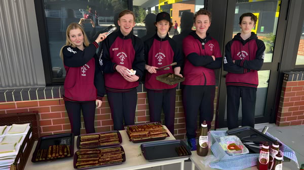 Fünf Schülerinnen und Schüler der Mount Compass Area School stehen in einheitlichen burgunderfarbenen Uniformen vor einem Laden mit Lebensmitteln und Ausrüstung.