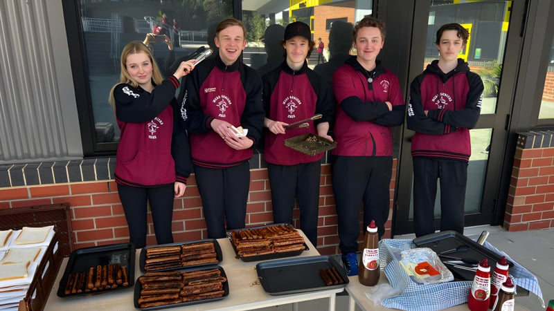 Fünf Schülerinnen und Schüler der Mount Compass Area School stehen in einheitlichen burgunderfarbenen Uniformen vor einem Laden mit Lebensmitteln und Ausrüstung.