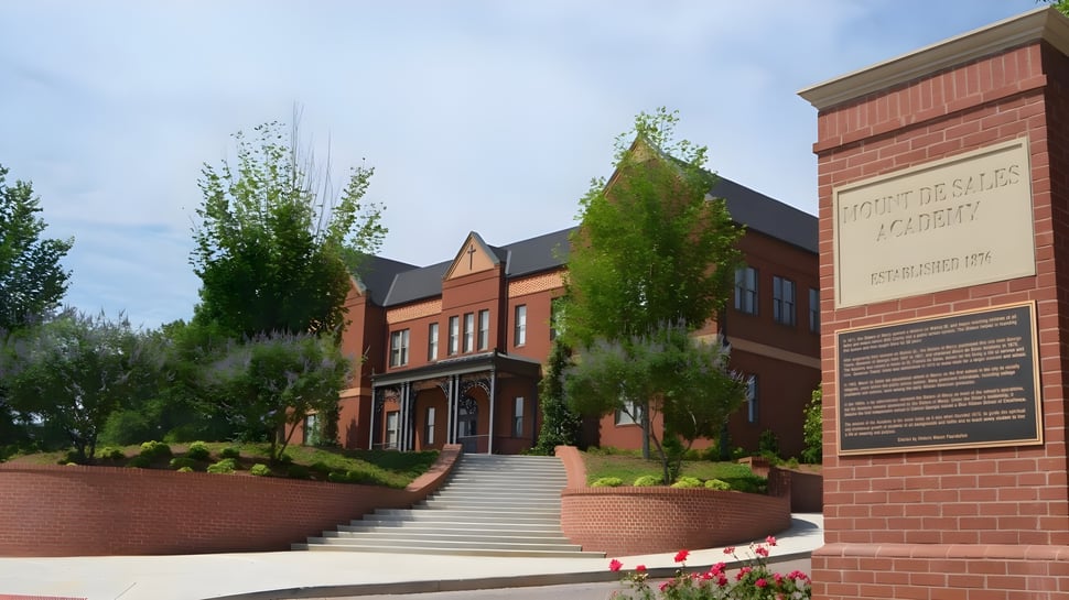 Das Backsteingebäude mit dem markanten Eingang der Mount De Sales Academy ist von grünen Pflanzen und einer Treppe umgeben.