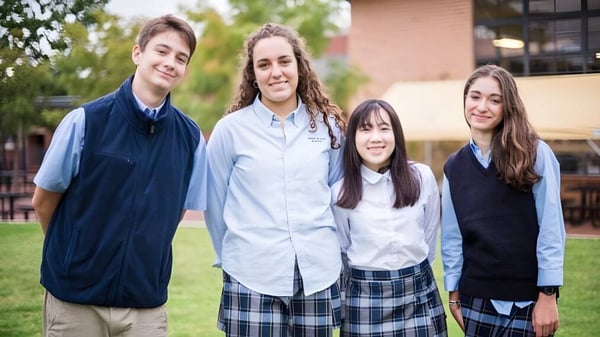 Eine Gruppe von vier Schülern steht gemeinsam im Außenbereich der Mount De Sales Academy mit Bäumen und Gebäuden im Hintergrund.