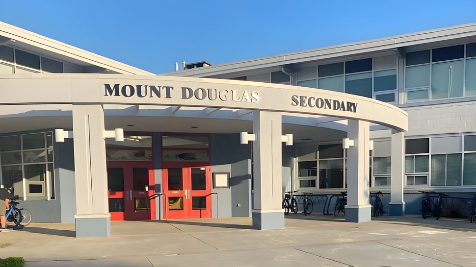 Das moderne zweistöckige Schulgebäude der Mount Douglas Secondary School mit roten Eingangstüren und blauem Himmel im Hintergrund.