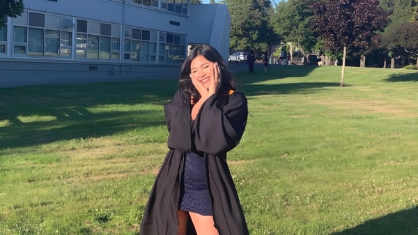 Eine junge Frau im schwarzen Mantel steht auf einer Wiese vor dem Gebäude der Mount Douglas Secondary School.