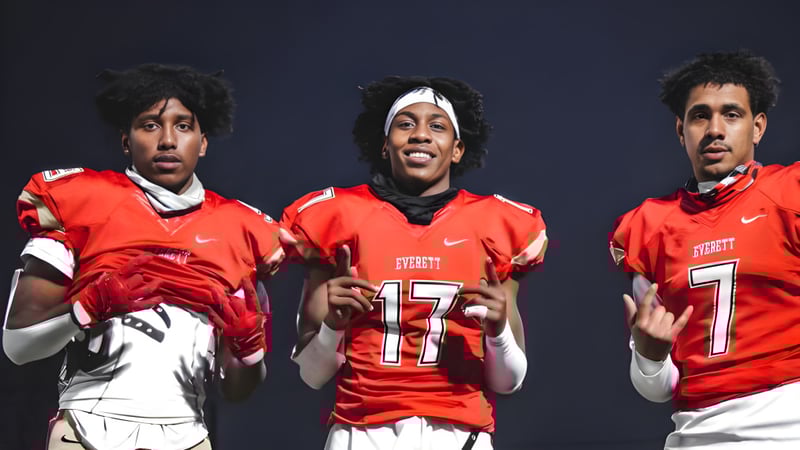 Drei Schülerinnen und Schüler der Mount Everett Regional High School tragen rote Football-Trikots mit den Nummern 17 und 7 vor dunklem Hintergrund.