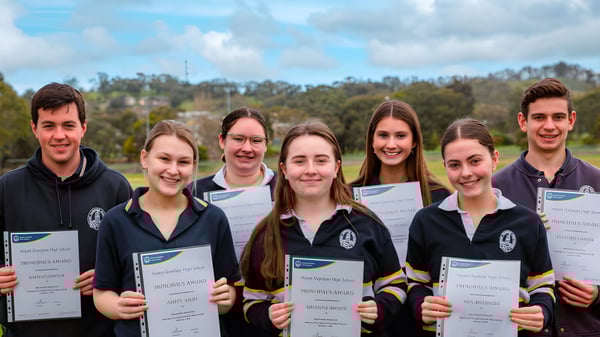 Schüler der Mount Gambier High School zeigen im Freien ihre Zertifikate vor Bäumen und Schulgebäuden.
