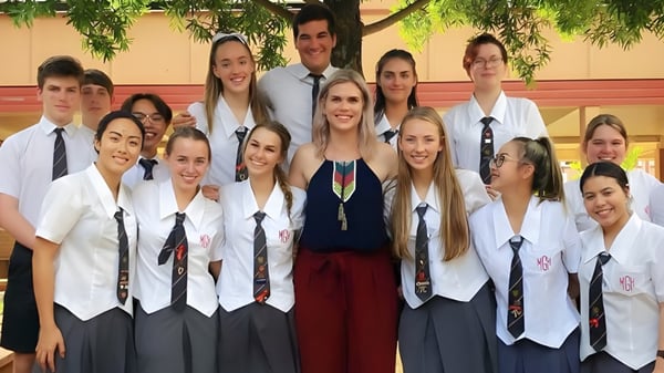 Eine Gruppe Schülerinnen und Schüler der Mount Gravatt State High School steht in einem Klassenraum mit einem grünen Baum im Hintergrund.