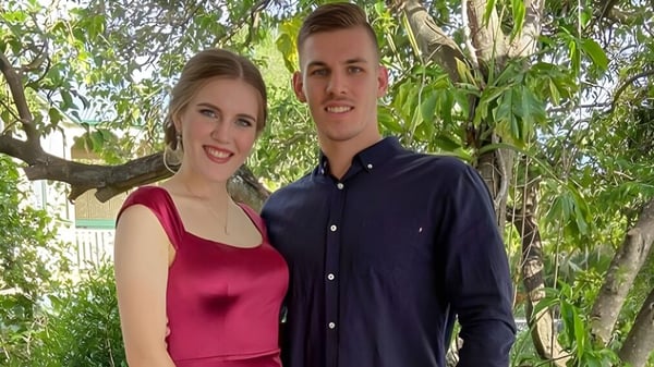 Ein lächelndes junges Paar steht draußen im Grünen auf dem Campus der Mount Gravatt State High School.