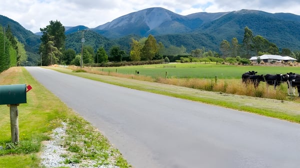 Eine gewundene Schotterstraße führt durch eine grüne Wiese mit Blick auf schneebedeckte Berge und dichte Wälder auf dem Gelände von Mount Hutt College.