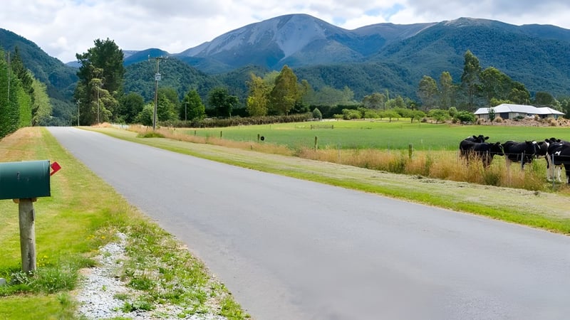 Eine gewundene Schotterstraße führt durch eine grüne Wiese mit Blick auf schneebedeckte Berge und dichte Wälder auf dem Gelände von Mount Hutt College.