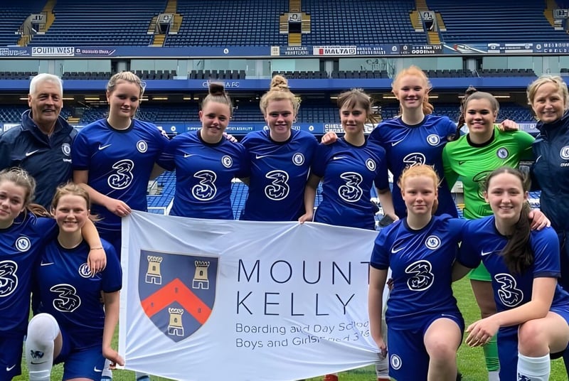 Eine Gruppe von Fußballspielerinnen posiert auf dem Spielfeld mit einem Banner der Mount Kelly School.