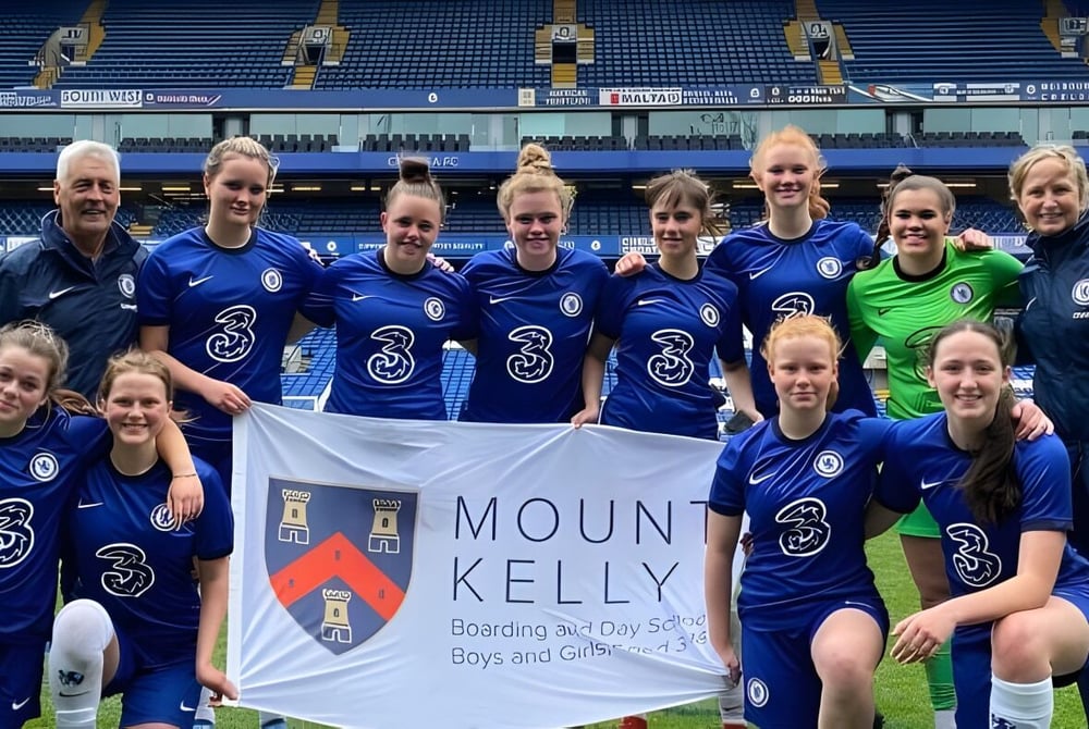 Eine Gruppe von Fußballspielerinnen posiert auf dem Spielfeld mit einem Banner der Mount Kelly School.