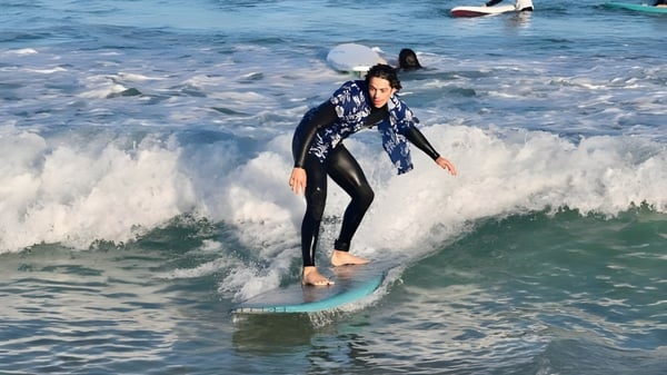 Eine Person in einem Neoprenanzug surft eine Welle im Ozean vor der Küste der Mount Lawley Senior High School.