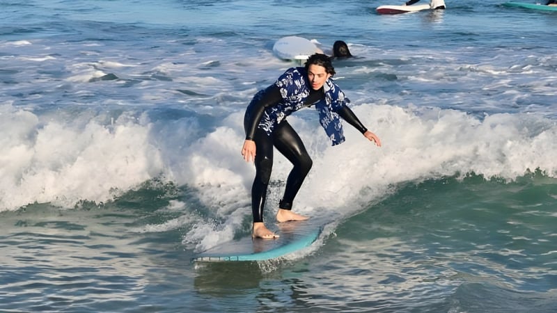 Eine Person in einem Neoprenanzug surft eine Welle im Ozean vor der Küste der Mount Lawley Senior High School.
