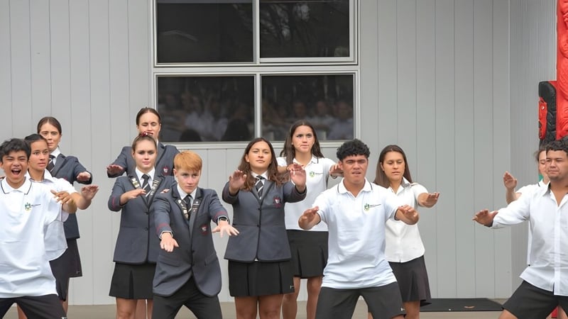 Eine Gruppe von Schülerinnen und Schülern steht vor einem Gebäude und applaudiert auf dem Campus des Mount Maunganui College.