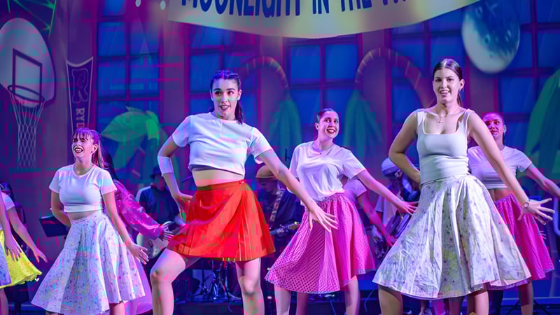 Eine Gruppe von Schülerinnen und Schülern des Mount Maunganui College führt auf einer Bühne mit neonbeleuchtetem Hintergrund einen Tanz auf.