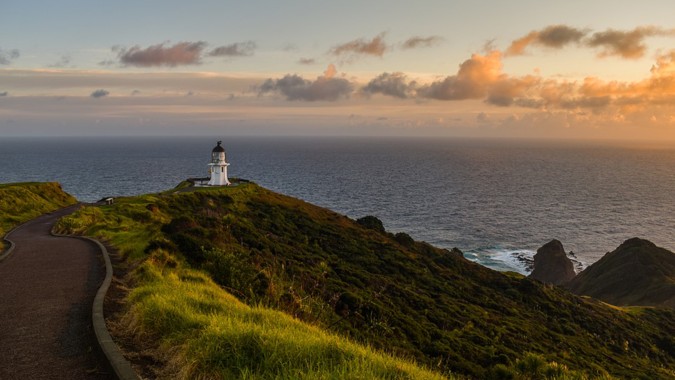Ein Leuchtturm steht auf einer steilen Klippe mit Gras und blickt auf den Ozean bei Sonnenuntergang auf dem Gelände von Mount Roskill Grammar.