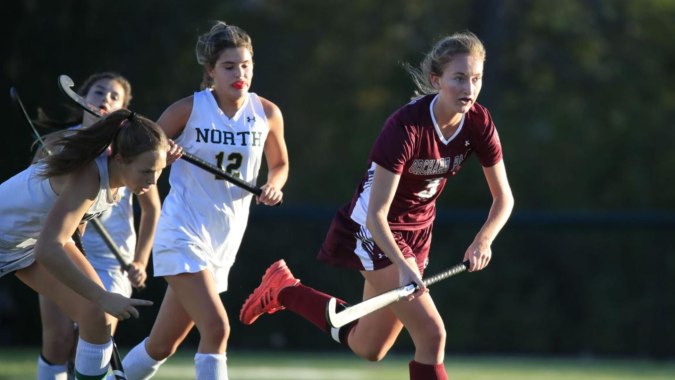 Drei Schülerinnen der Mount Sackville Secondary School spielen Sport auf einem Rasenfeld vor Bäumen.