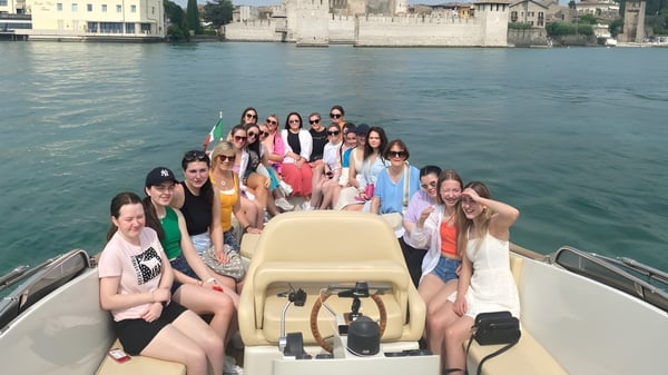 Eine Gruppe junger Frauen sitzt auf einem Boot im Wasser vor der historischen Skyline von Mount Saint Michael.