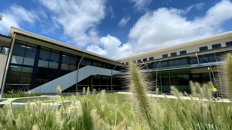 Ein modernes Gebäude aus Glas und Beton mit einer Rasenfläche davor auf dem Campus der Mount Saint Michael Schule unter blauem Himmel mit weißen Wolken.
