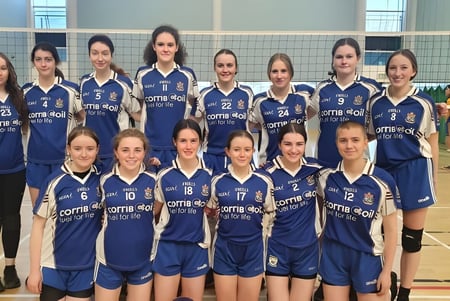 Eine Gruppe junger Volleyballspielerinnen in blauen Trikots posiert in der Sporthalle der Mount Saint Michael School.