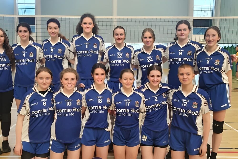 Eine Gruppe junger Volleyballspielerinnen in blauen Trikots posiert in der Sporthalle der Mount Saint Michael School.