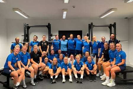 Eine Gruppe von Schülern der The Mount School York posiert in blauen Uniformen in der Trainingshalle mit Sportgeräten.