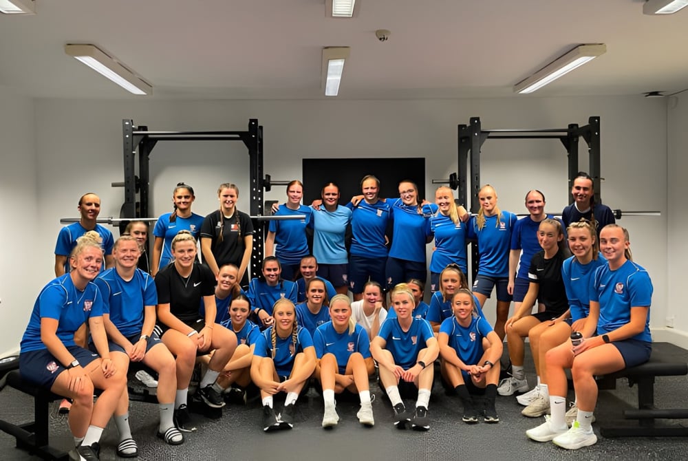 Eine Gruppe von Schülern der The Mount School York posiert in blauen Uniformen in der Trainingshalle mit Sportgeräten.