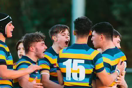 Eine Gruppe von Rugby spielenden Schülern im farbigen Trikot auf dem Gelände von Mount St. Mary's College steht eng zusammen.