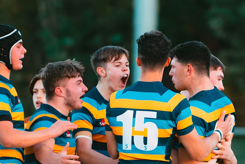 Eine Gruppe von Rugby spielenden Schülern im farbigen Trikot auf dem Gelände von Mount St. Mary's College steht eng zusammen.