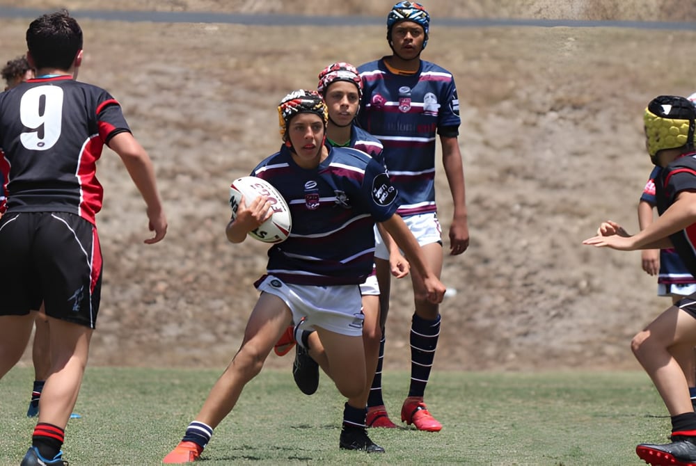Schüler der Mountain Creek State High School spielen ein Rugbyspiel auf einem Spielfeld mit grünem Gras unter blauem Himmel.