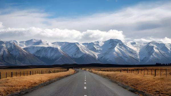 Eine gewundene Straße führt durch ein goldenes Feld zu schneebedeckten Bergen unter einem bewölkten Himmel bei der Mountainview High School.