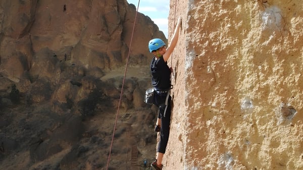 Ein Schüler der Mount Boucherie Secondary School klettert mit Ausrüstung an einer steilen Felswand in natürlicher Umgebung.