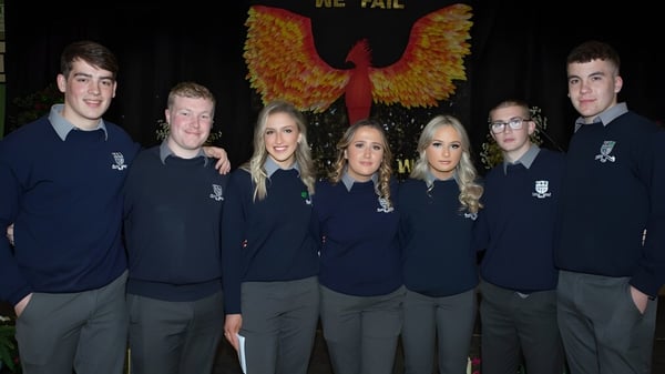 Eine Gruppe Schüler der Mountmellick Community School steht vor einem großen phönixartigen Emblem auf dunklem Hintergrund.