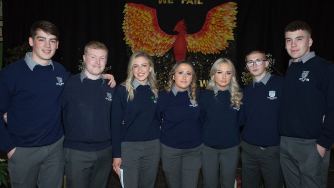 Eine Gruppe von Schülerinnen und Schülern in dunkelblauen Uniformen mit Phoenix-Emblem im Hintergrund auf dem Campus der Mountmellick Community School.