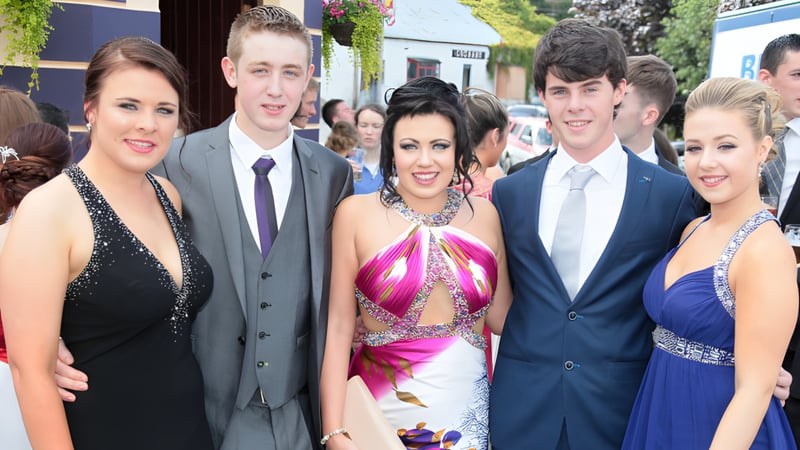 Eine Gruppe in formeller Kleidung posiert bei einer Veranstaltung auf dem Campus der Moyne Community School vor Gebäuden und Grünflächen.