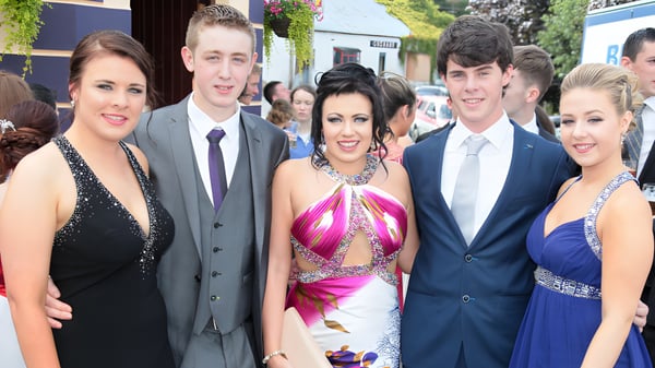 Eine Gruppe in formeller Kleidung posiert bei einer Veranstaltung auf dem Campus der Moyne Community School vor Gebäuden und Grünflächen.