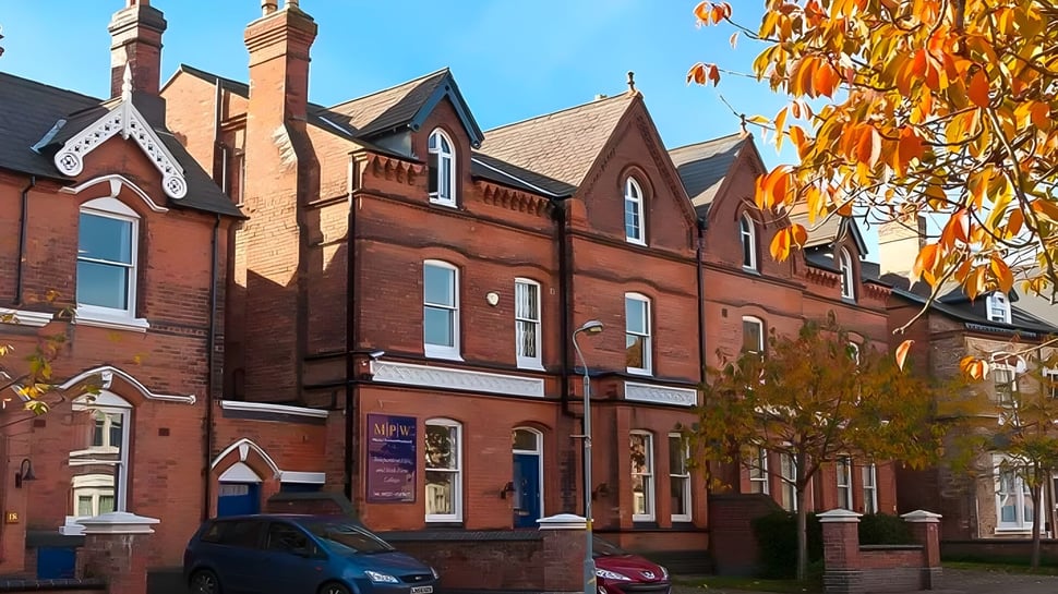 Das mehrstöckige Backsteingebäude mit verzierter Architektur der MPW Birmingham ist von buntem Herbstlaub umgeben.
